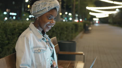 Retrato-De-Una-Alegre-Mujer-Afroamericana-Con-Una-Laptop-En-El-Parque-Por-La-Noche